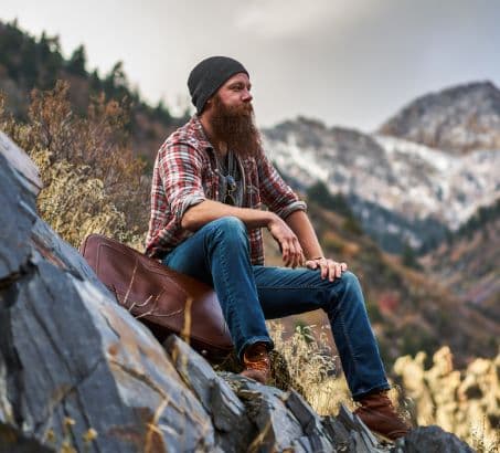 Bearded man sitting on a stony hillside surrounded by nature and mountains in the distance