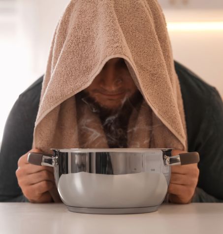 man doing steam treatment over a bowl of hot water with towel on his head
