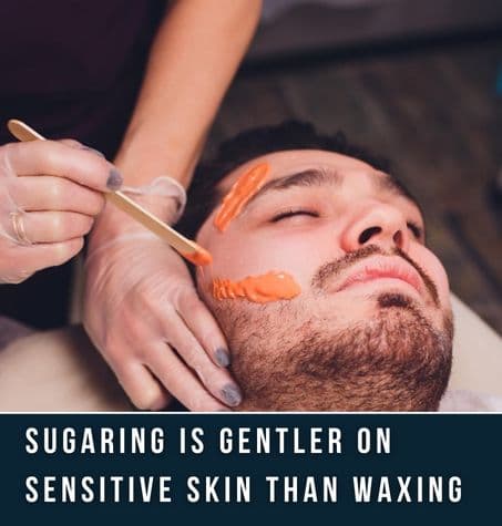 therapist applying sugaring paste onto a bearded client.Text overlay reads sugaring is gentler on sensitive skin than waxing