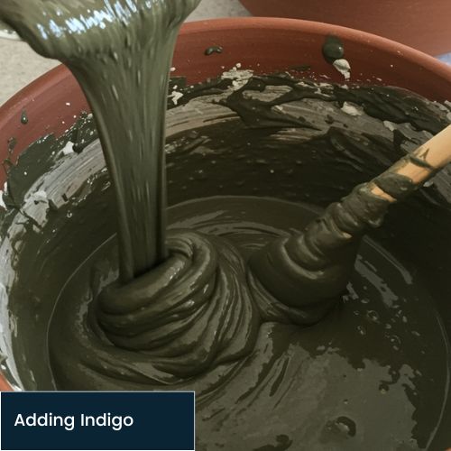 adding indigo paste to henna paste in a bowl and stirring with wooden spoon