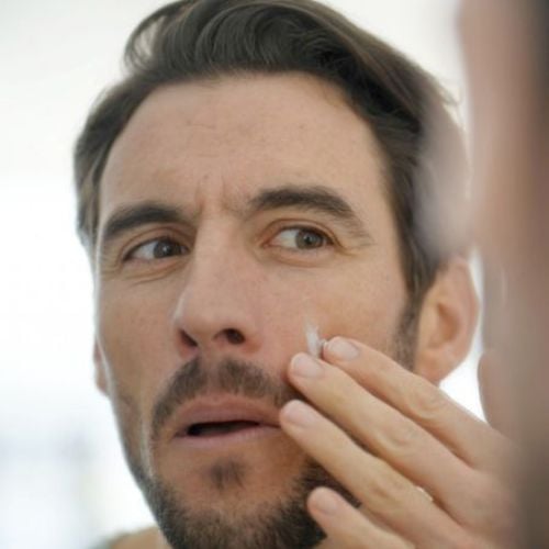 man applying face moisturiser in front of a mirror