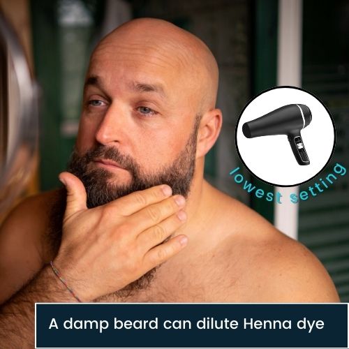 man touching his beard to check for dampness, a hairdryer on the lowest setting