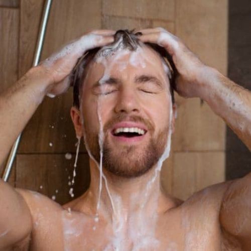man washing his hair in the shower with hair shampoo