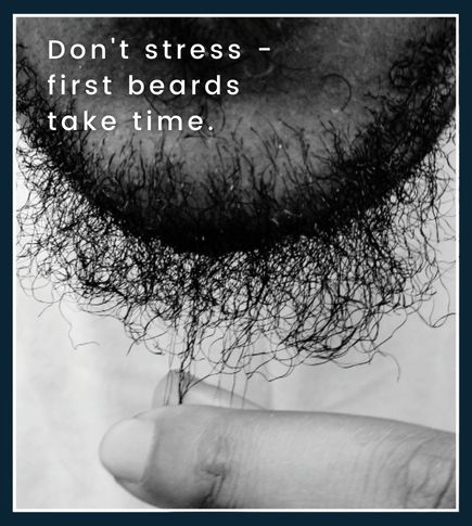 Close up of a man with a patchy beard, he is gently tugging at a few beard hairs symbolizing that early beard growth is normal and takes time
