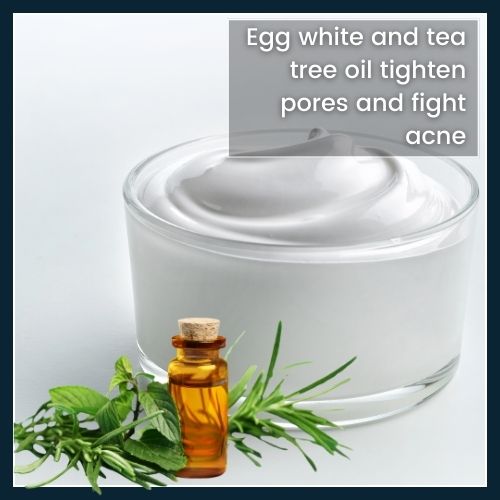 Flat-lay of a bowl with whipped egg white and a small bottle of tea tree oil, illustrating a DIY mask that tightens pores and combats acne.