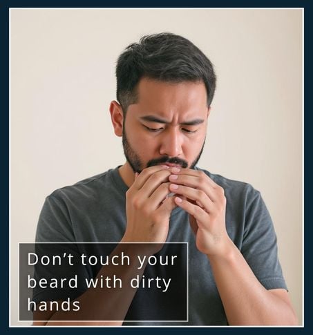 Man about to touch his beard, pausing to look at slightly dirty hands