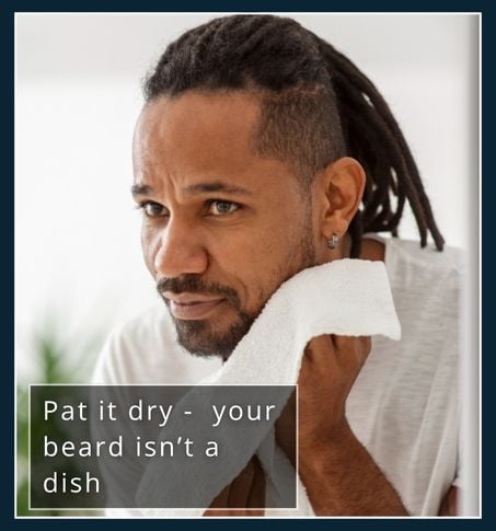 Man gently patting his beard dry with a towel after washing