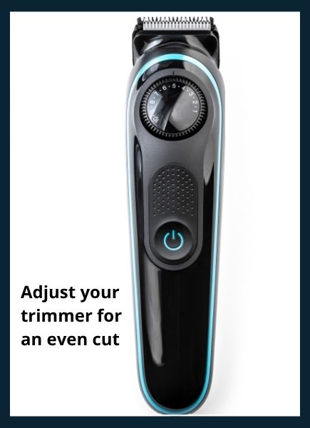 Black electric beard trimmer with adjustable comb guard and stainless steel blades on a wooden countertop with small hair clippings