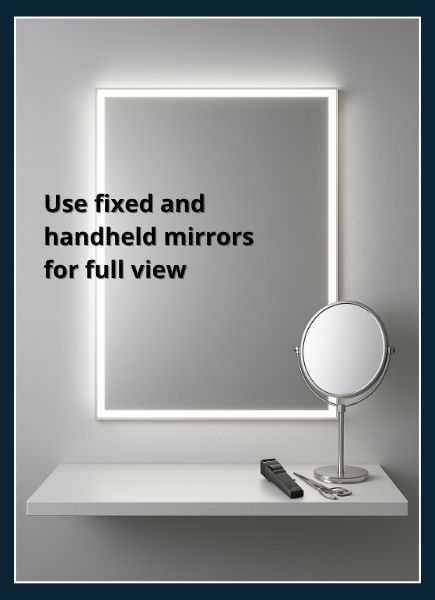 Wall‑mounted mirror framed by white LED lights with a handheld mirror resting on a nearby shelf angled to view the neck area
