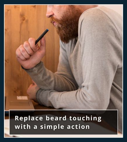 A man at a desk holding a pen in his hand instead of touching his beard, breaking the habit with a replacement action.