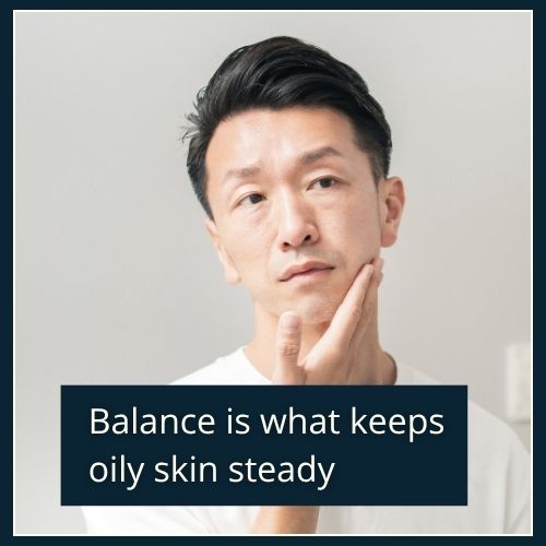 A man with a fresh, matte complexion standing near a mirror looking at his reflection with a calm, content expression