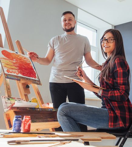 A man and woman painting together in a bright art studio, laughing and enjoying a relaxed creative date.