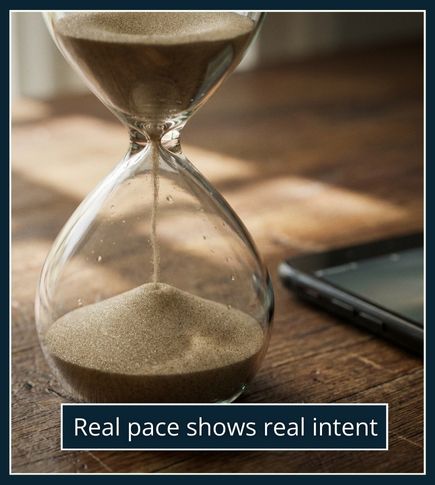 A close-up of an hourglass beside a resting phone on a desk, symbolising patience and taking time to see someone’s real intentions.