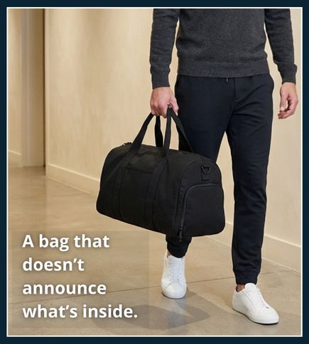Man standing indoors carrying a small black gym bag in a clean modern setting, suitable for gym and everyday use