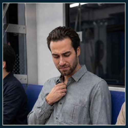 man sitting on train has realised that the weird smell is coming from his shirt.