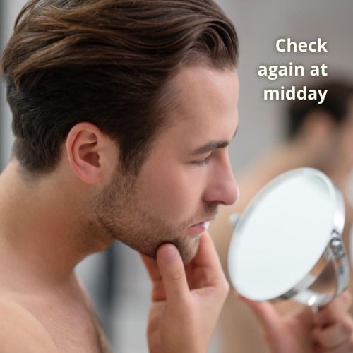 a man uses a hand mirror to access his double chin in the morning. He is checking whether the his double chin is caused by water retention.