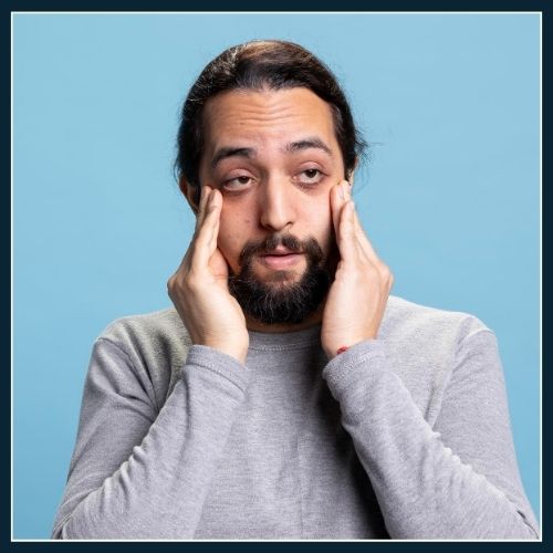 man with a drawn and tired looking face, giving himself a light massage around his eye area.