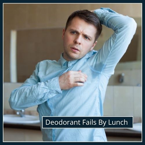 Business man at work checks his armpits in the bathroom and notices sweat patches on his shirt.
