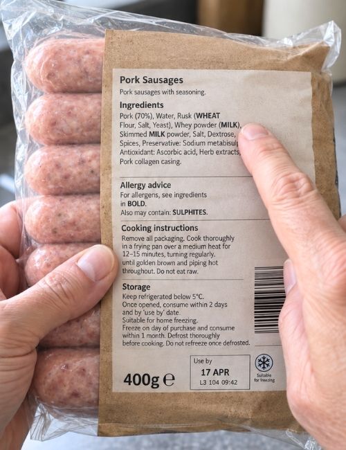 Man checking the back of a packet of sausages for signs of dairy.